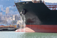 Large Anchored Cargo Ship Discharging Ballast Water Out From Anchor's Hub.