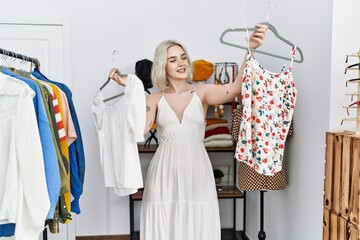 Poster - Young caucasian woman smiling confident holding clothes at clothing store