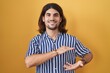 © Krakenimages.com - Hispanic man with long hair standing over yellow background gesturing with hands showing big and large size sign, measure symbol. smiling looking at the camera. measuring concept.
