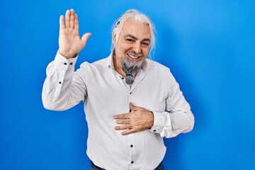 Poster - Middle age man with grey hair standing over blue background waiving saying hello happy and smiling, friendly welcome gesture