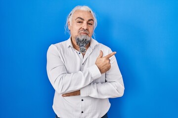 Poster - Middle age man with grey hair standing over blue background pointing with hand finger to the side showing advertisement, serious and calm face