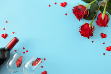 Love Holiday Concept. Flat Lay Composition Made Of Red Roses, Wine Bottle With Glasses, Red Hearts On Pastel Blue Background With Copy Space In The Middle. Mother's Day Or Valentines Idea.