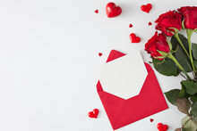Valentines Day Concept. Top View Photo Of Open Envelope With White Card, Red Flowers And Shaped Hearts On White Background With Copy Space. Lovers Holiday Card Idea.