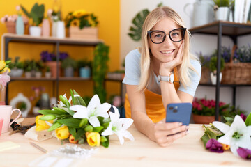 Canvas Print - Young blonde woman florist using smartphone leaning on table at flower shop