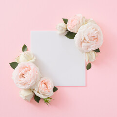 Wall Mural - Top view of spring flowers with green leaves and white frame on pastel pink background. Minimal flat lay nature background. Valentines or woman's day concept.