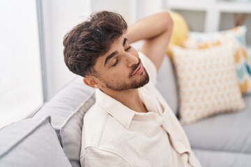 Sticker - Young arab man relaxed with hand on head sitting on sofa at home