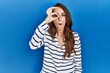 © Krakenimages.com - Young hispanic woman standing over blue isolated background doing ok gesture shocked with surprised face, eye looking through fingers. unbelieving expression.