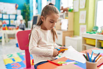 Poster - Adorable hispanic girl student sitting on table cutting paper at kindergarten