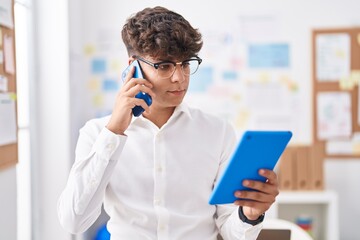 Poster - Young hispanic teenager business worker talkiong on smartphone using touchpad at office