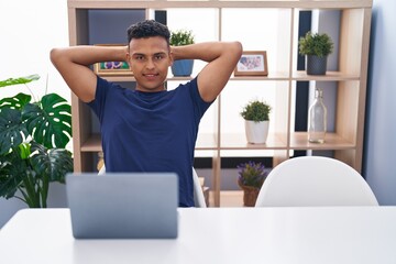 Wall Mural - Young latin man using laptop relaxed with hands on head at home