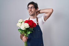 Young Hispanic Man Holding Bouquet Of White And Red Roses Smiling Confident Touching Hair With Hand Up Gesture, Posing Attractive And Fashionable