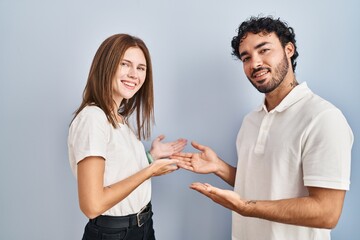 Canvas Print - Young couple wearing casual clothes standing together inviting to enter smiling natural with open hand