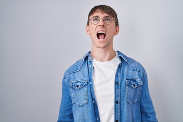 Poster - Caucasian blond man standing wearing glasses angry and mad screaming frustrated and furious, shouting with anger. rage and aggressive concept.