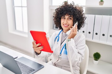 Canvas Print - Young middle east woman wearing doctor uniform using touchpad talking on telephone at clinic