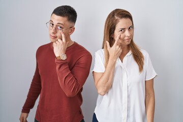 Sticker - Mother and son standing together over isolated background pointing to the eye watching you gesture, suspicious expression