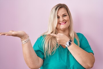 Sticker - Caucasian plus size woman standing over pink background amazed and smiling to the camera while presenting with hand and pointing with finger.