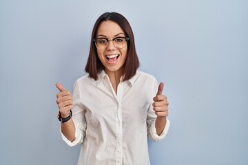 Sticker - Young hispanic woman standing over white background success sign doing positive gesture with hand, thumbs up smiling and happy. cheerful expression and winner gesture.