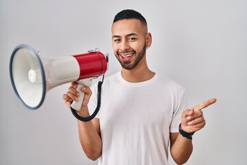 Sticker - Young hispanic man shouting through megaphone smiling happy pointing with hand and finger to the side