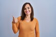© Krakenimages.com - Middle age brunette woman standing wearing orange sweater doing happy thumbs up gesture with hand. approving expression looking at the camera showing success.