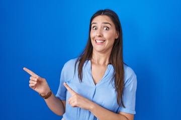 Sticker - Young brunette woman standing over blue background pointing aside worried and nervous with both hands, concerned and surprised expression