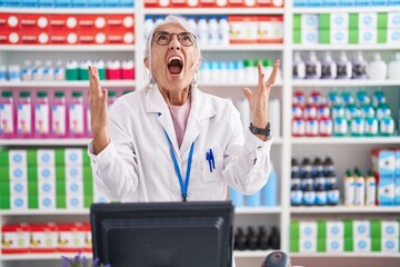 Poster - Middle age woman with tattoos working at pharmacy drugstore crazy and mad shouting and yelling with aggressive expression and arms raised. frustration concept.