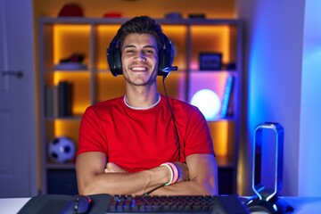 Wall Mural - Young hispanic man playing video games happy face smiling with crossed arms looking at the camera. positive person.