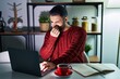 © Krakenimages.com - Young hispanic man with beard using computer laptop at night at home smelling something stinky and disgusting, intolerable smell, holding breath with fingers on nose. bad smell