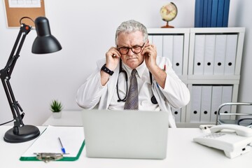 Poster - Senior caucasian man wearing doctor uniform and stethoscope at the clinic covering ears with fingers with annoyed expression for the noise of loud music. deaf concept.