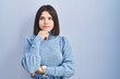 © Krakenimages.com - Young hispanic woman standing over blue background with hand on chin thinking about question, pensive expression. smiling and thoughtful face. doubt concept.
