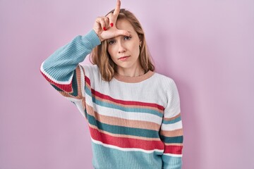 Canvas Print - Young blonde woman standing over pink background making fun of people with fingers on forehead doing loser gesture mocking and insulting.