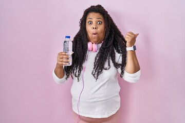 Poster - Plus size hispanic woman wearing sportswear and headphones surprised pointing with hand finger to the side, open mouth amazed expression.