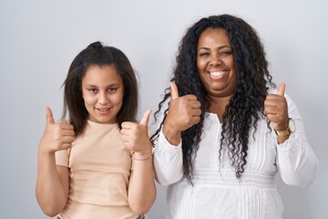 Poster - Mother and young daughter standing over white background success sign doing positive gesture with hand, thumbs up smiling and happy. cheerful expression and winner gesture.