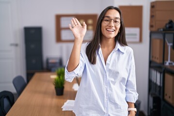 Canvas Print - Young hispanic woman at the office waiving saying hello happy and smiling, friendly welcome gesture