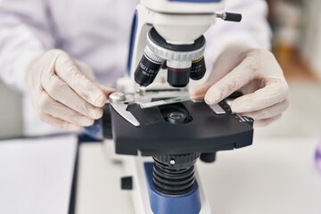 Poster - Middle age hispanic woman wearing scientist uniform using microscope at laboratory