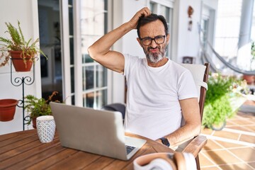 Wall Mural - Middle age man using computer laptop at home confuse and wondering about question. uncertain with doubt, thinking with hand on head. pensive concept.