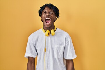 Sticker - Young african man with dreadlocks standing over yellow background angry and mad screaming frustrated and furious, shouting with anger. rage and aggressive concept.