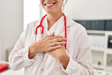 Wall Mural - Young blonde woman wearing doctor uniform standing with hands on heart at clinic