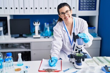 Sticker - Young hispanic woman scientist write on document using microscope at laboratory