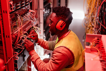 Side view portrait of technician setting up network in server room and wearing ear protection lit by red neon lights