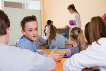 Happy pupils chattering sitting on back desks at lesson in elementary school