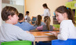 Happy pupils chattering sitting on back desks at lesson in elementary school