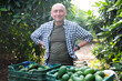 Portrait of happy man owner of farm standing with box of freshly picked avocados in garden during harvest
