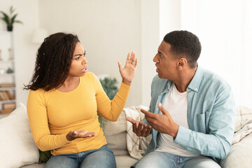 Wall Mural - Angry sad emotional young african american lady and male screaming, gesturing, sitting on sofa