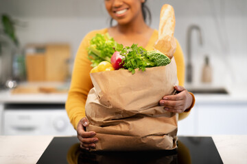 Wall Mural - Smiling young african american female hold paper bag with groceries in modern kitchen interior