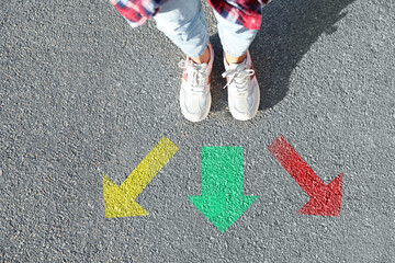 Wall Mural - Choice of way. Woman standing in front of drawn marks on road, closeup. Colorful arrows pointing in different directions