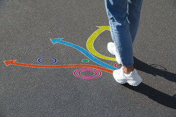 Choice of way. Woman walking towards drawn marks on road, closeup. Colorful arrows pointing in different directions