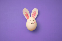 Food Photo. White Chicken Egg With Cute Rabbit Face And Bunny Ears On A Purple Background. Greeting Card For Religious Holiday Happy Easter. Preparation For The Celebration. Banner. Copyspace. Poster