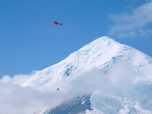 A Rescue Helicopter Of The Type A Star Is Performing A Longline Rescue Mission On Mount McKinley, Alaska. Beneath The Helicopter A Mountain Rescuer Is Dangling On A Rope. Mount For
