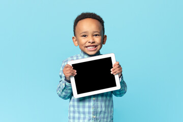 Cute african american kid boy holding digital tablet with blank black screen, recommending new app or website, mockup