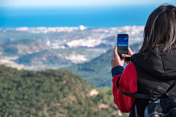 Joven mujer tomando fotos con su teléfono móvil desde lo alto de la montaña.